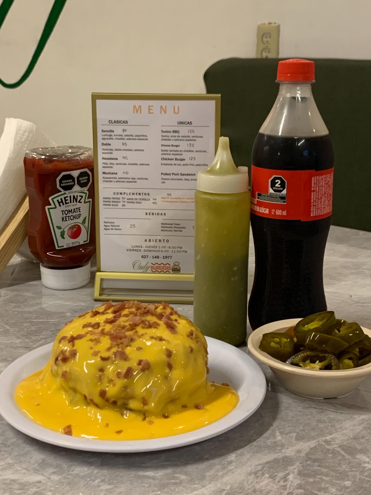 Cheese Burger de Only Burgers bañada en queso cheddar con bebida al fondo